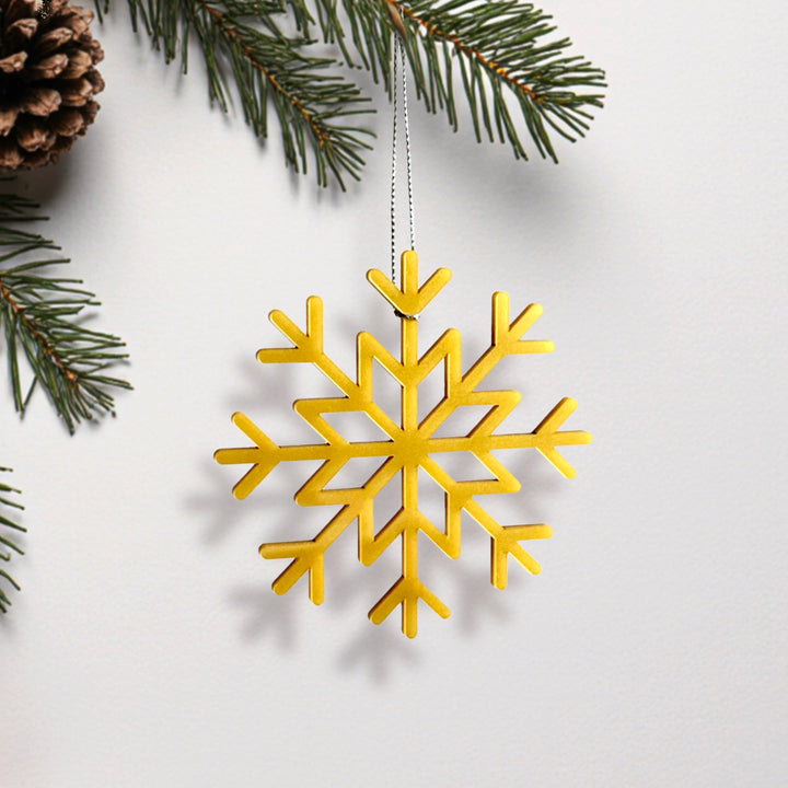 A golden snowflake ornament is hanging from a string, surrounded by pine branches and pine cones. A golden snowflake ornament is hanging from a string, surrounded by pine branches and pine cones.