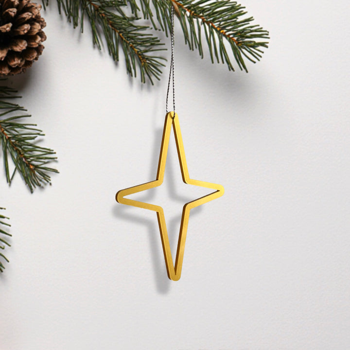 A golden star-shaped ornament is hanging from a branch of a pine tree, with pine needles and a pine cone visible in the background. A golden star-shaped ornament is hanging from a branch of a pine tree, with pine needles and a pine cone visible in the background.