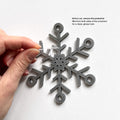 A hand is carefully removing a protective film from the sides of a silver snowflake ornament. - Photo #5
