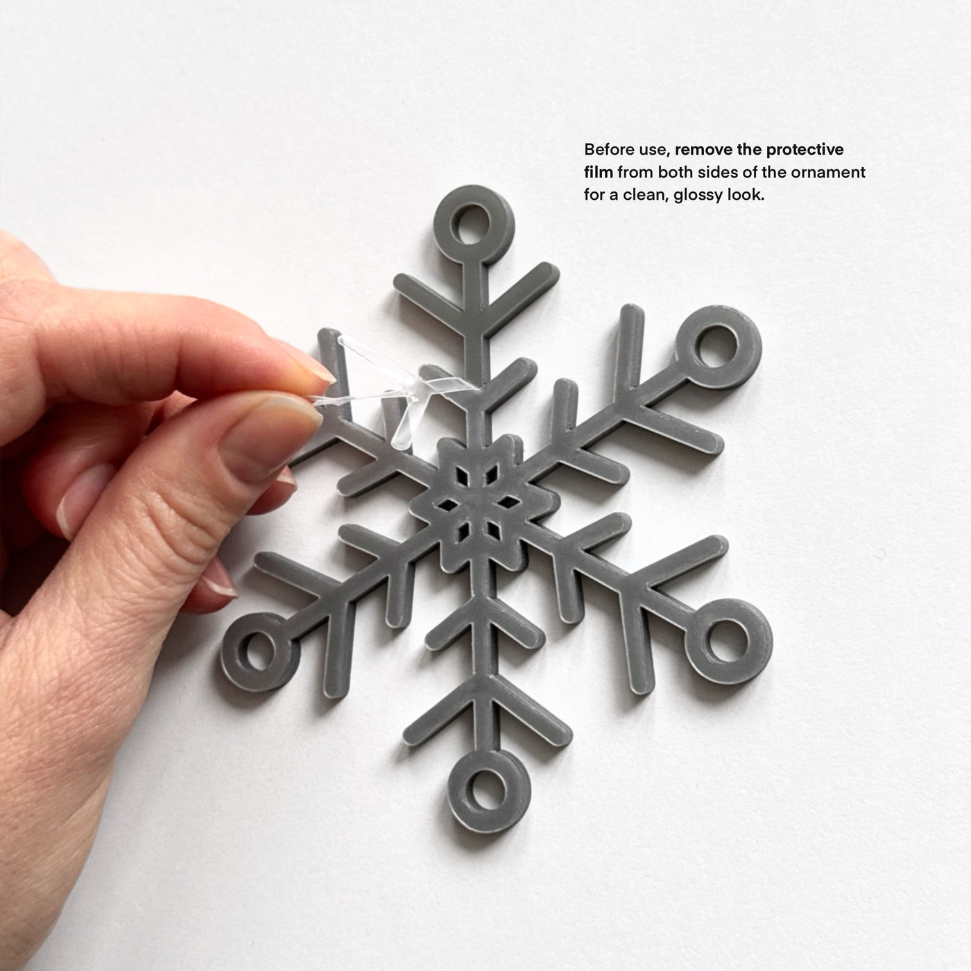 A hand is carefully removing a protective film from the sides of a silver snowflake ornament.