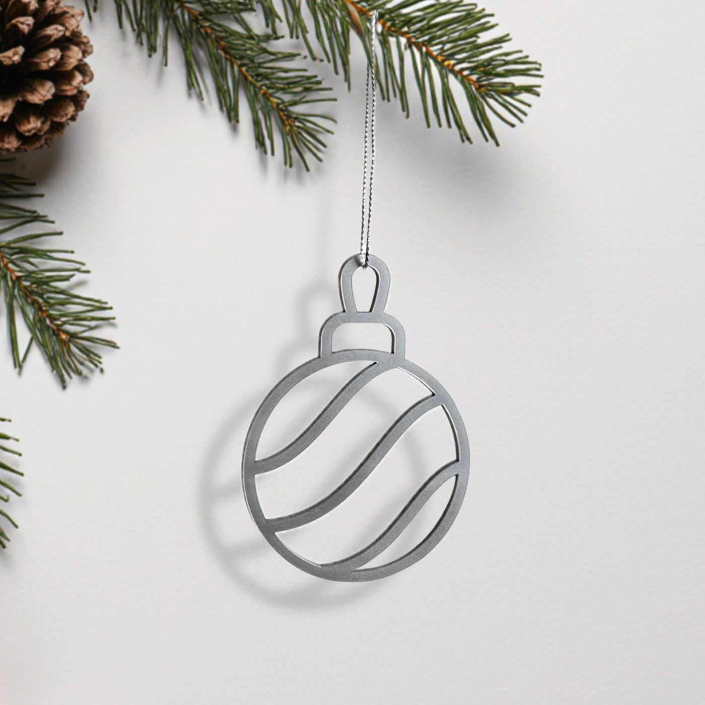 A silver ornament in the shape of a ball hangs from a branch of a pine tree.