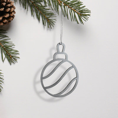 A silver ornament in the shape of a ball hangs from a branch of a pine tree.