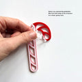 A hand is holding a red and white candy cane ornament, with instructions on how to remove the protective film from both sides of the ornament for a clean, glossy look. - Photo #5