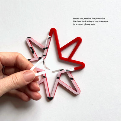 A hand is holding a red star-shaped ornament made of plastic, with instructions on how to remove the protective film from both sides for a clean, glossy look.