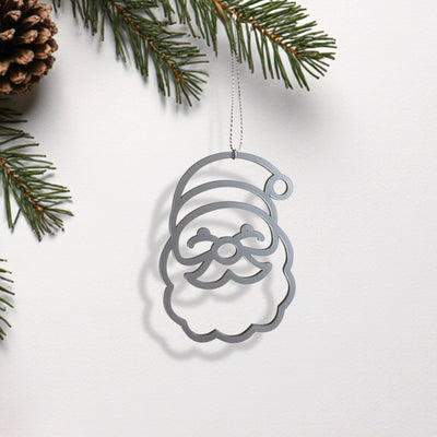 A silver ornament resembling a smiling face is hanging from a branch of a pine tree.