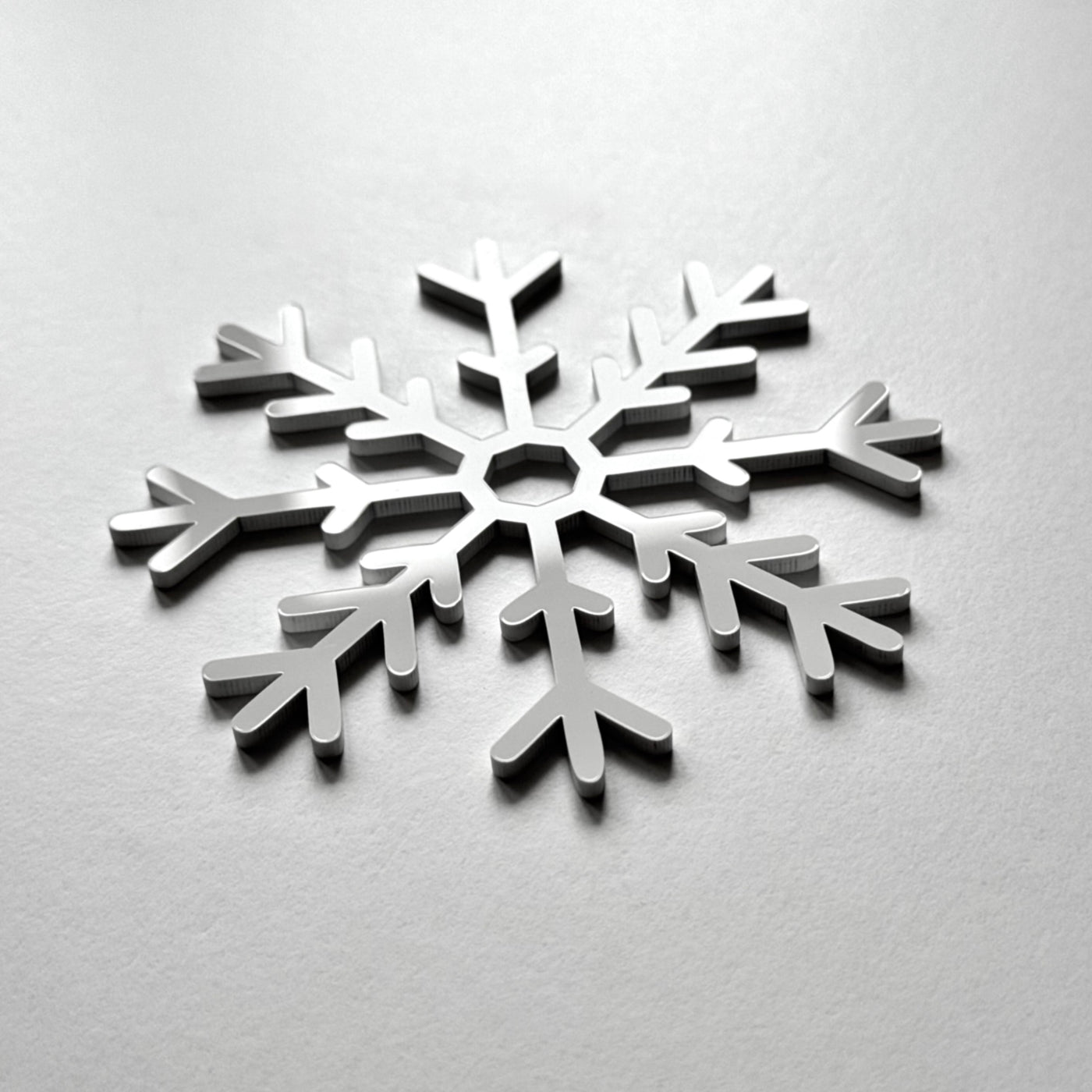 A silver snowflake-shaped object is centered on a plain white background.