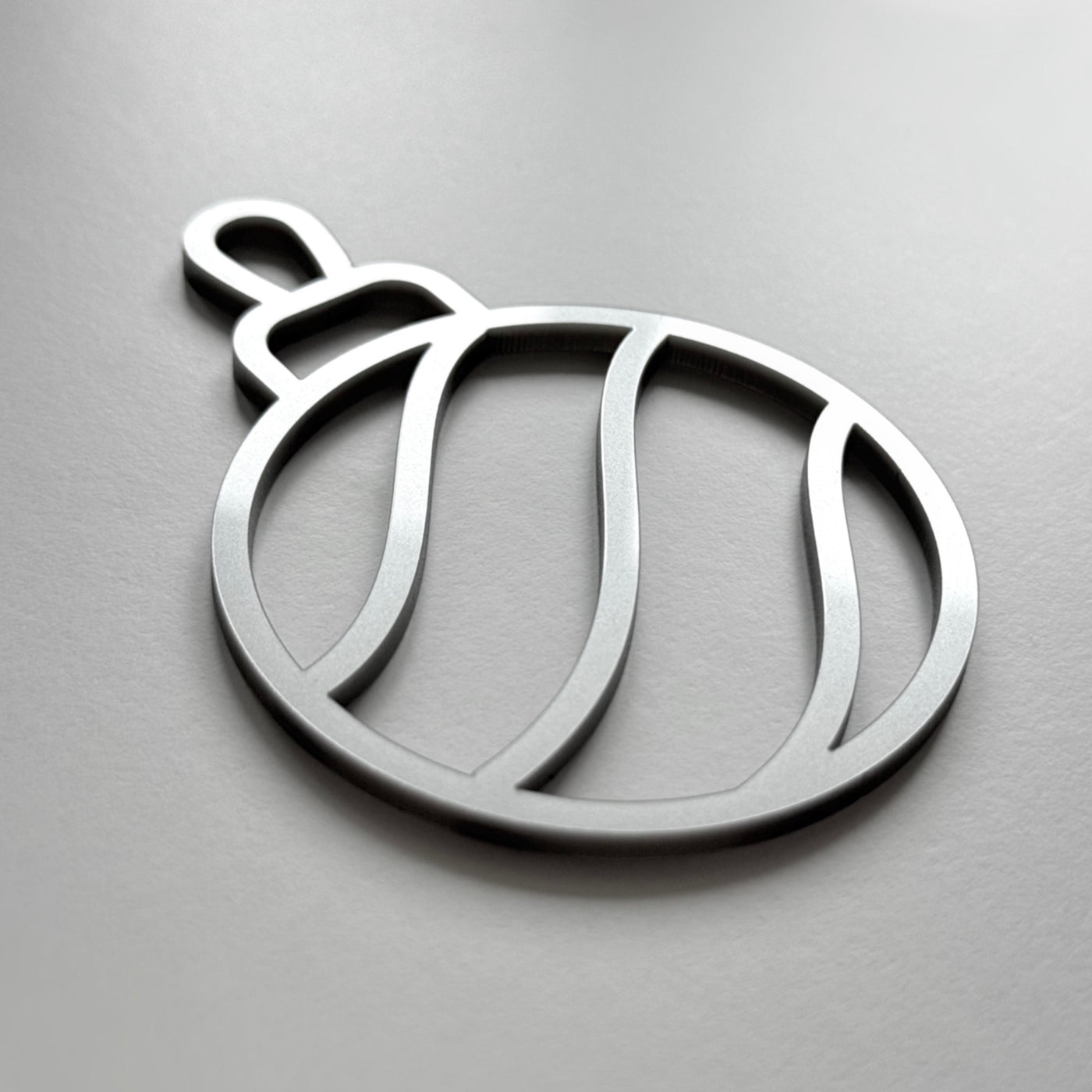 A simple, minimalist silver ornament or ornament-like shape is shown against a plain background.