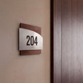 a sign with the number 204 on it, mounted on a wall next to a wooden door. - Photo #8