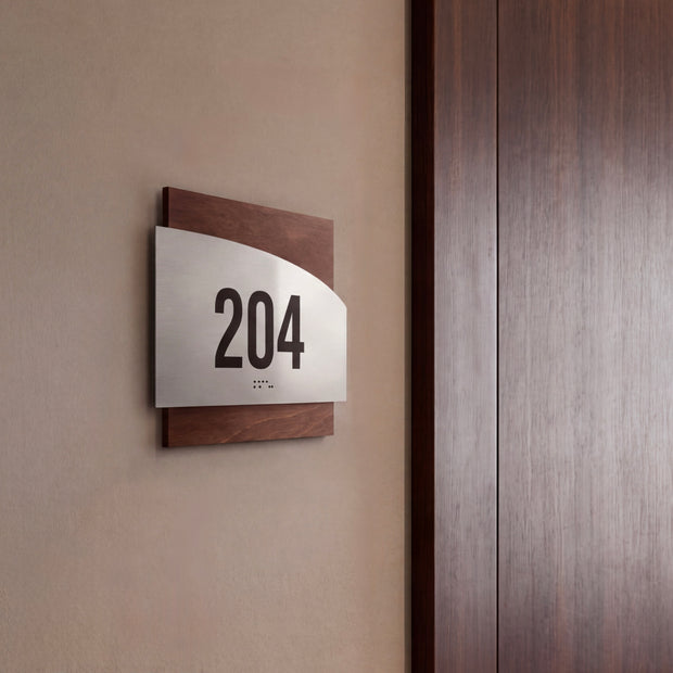 a sign with the number 204 on it, mounted on a wall next to a wooden door.