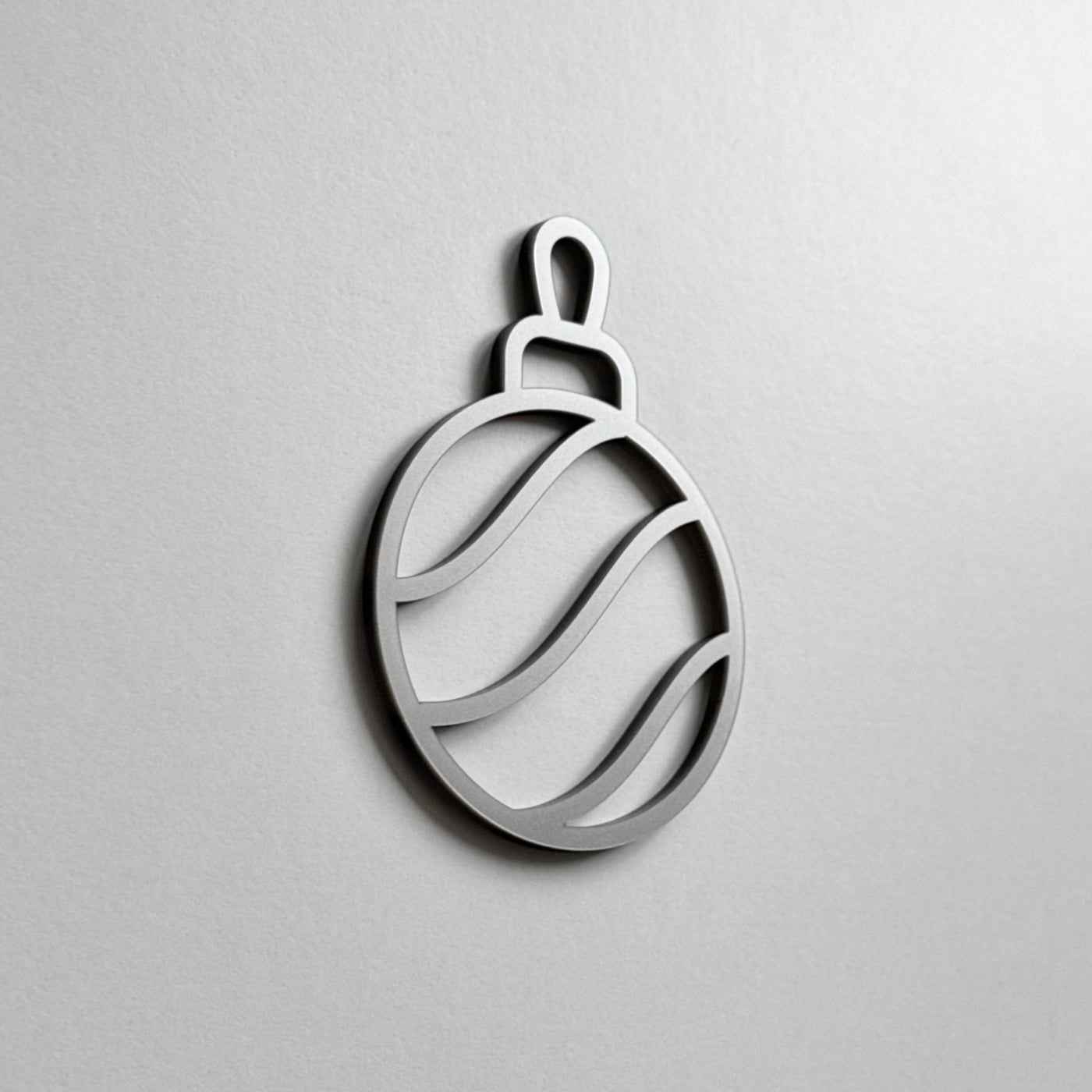 A simple, minimalist silver ornament or ornament-like shape is displayed against a plain white background.