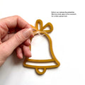 A hand is holding a yellow bell-shaped ornament with a clear plastic film on both sides, as indicated in the instructions. - Photo #4