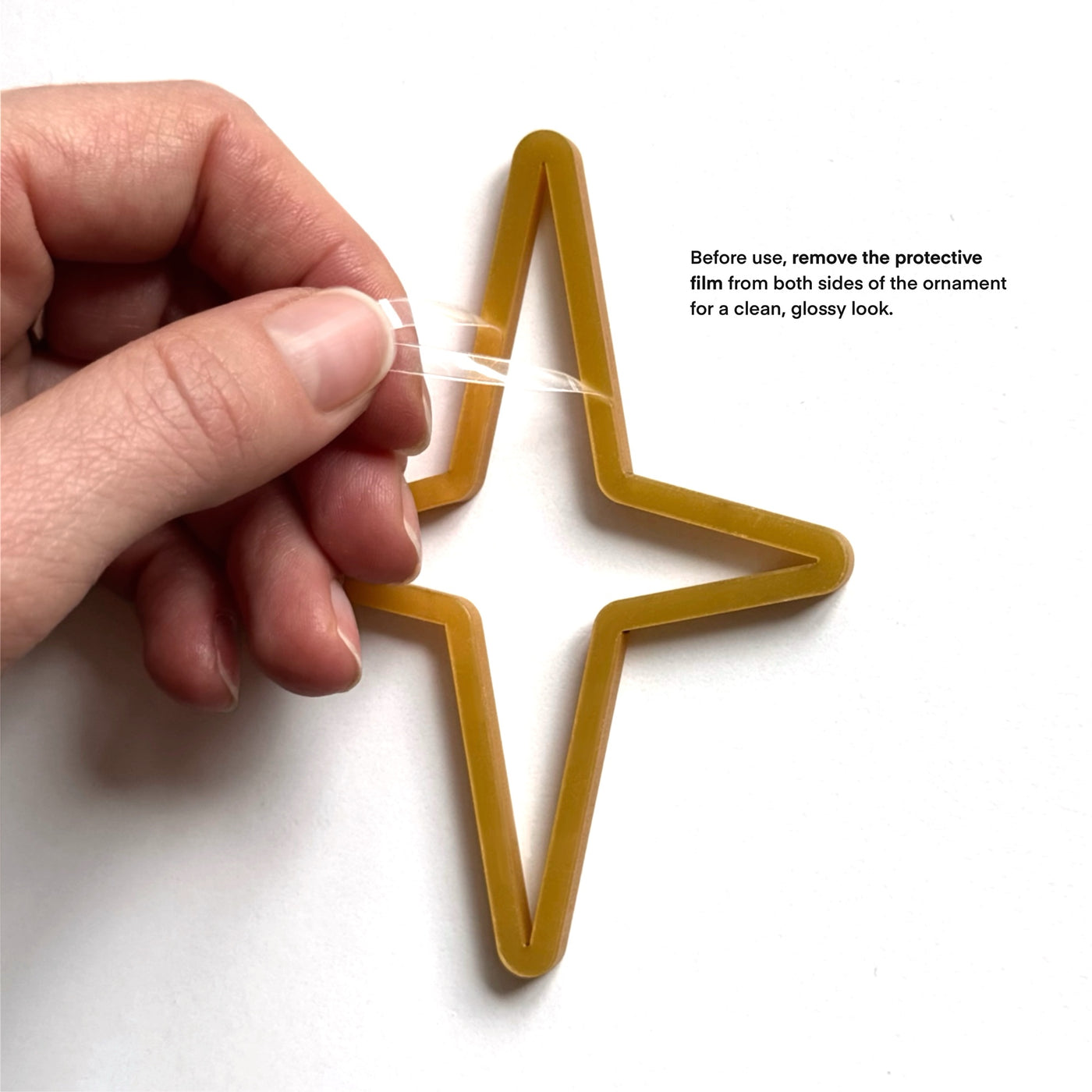 A hand is holding a star-shaped ornament made of a yellow material, with instructions on how to remove the protective film from both sides of the ornament for a clean, glossy look.
