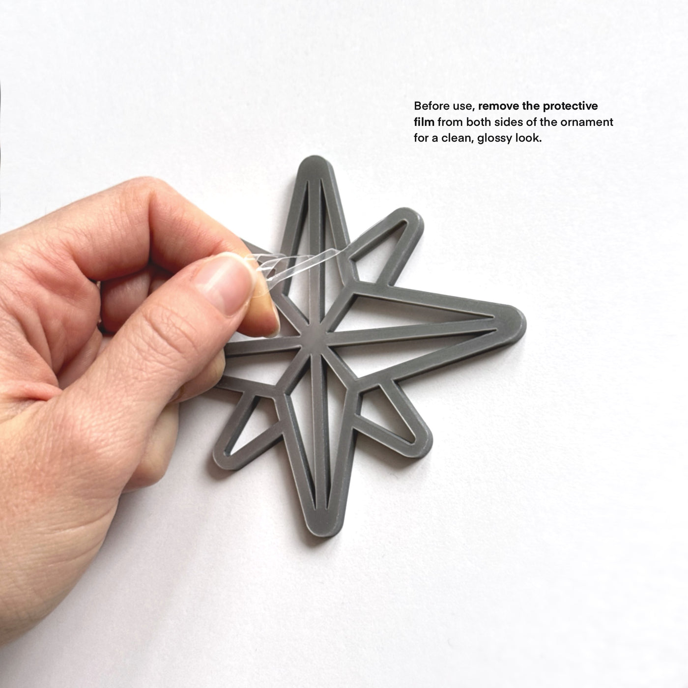 A hand is holding a star-shaped ornament made of a shiny material, with instructions on how to remove protective films from both sides for a clean, glossy look.