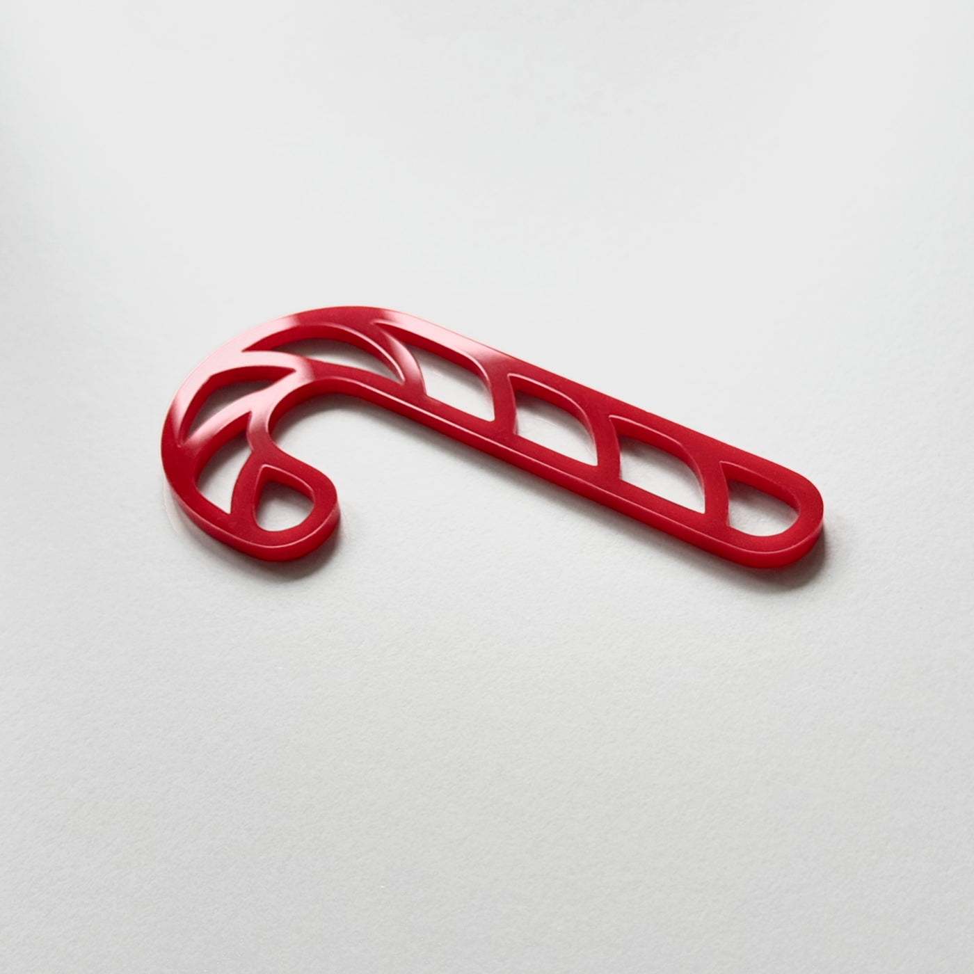 A red plastic candy cane decoration is shown against a plain white background.