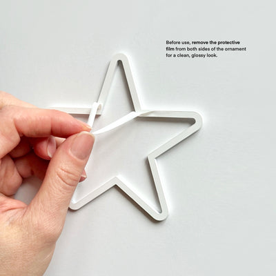 A hand is holding a white star-shaped ornament and removing a protective film from both sides of it.