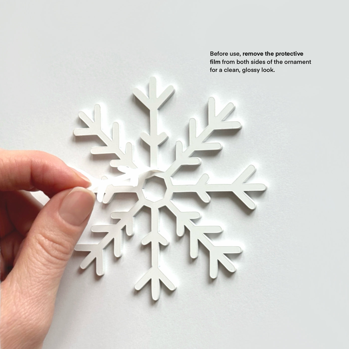 A hand is holding a white snowflake ornament against a white background.