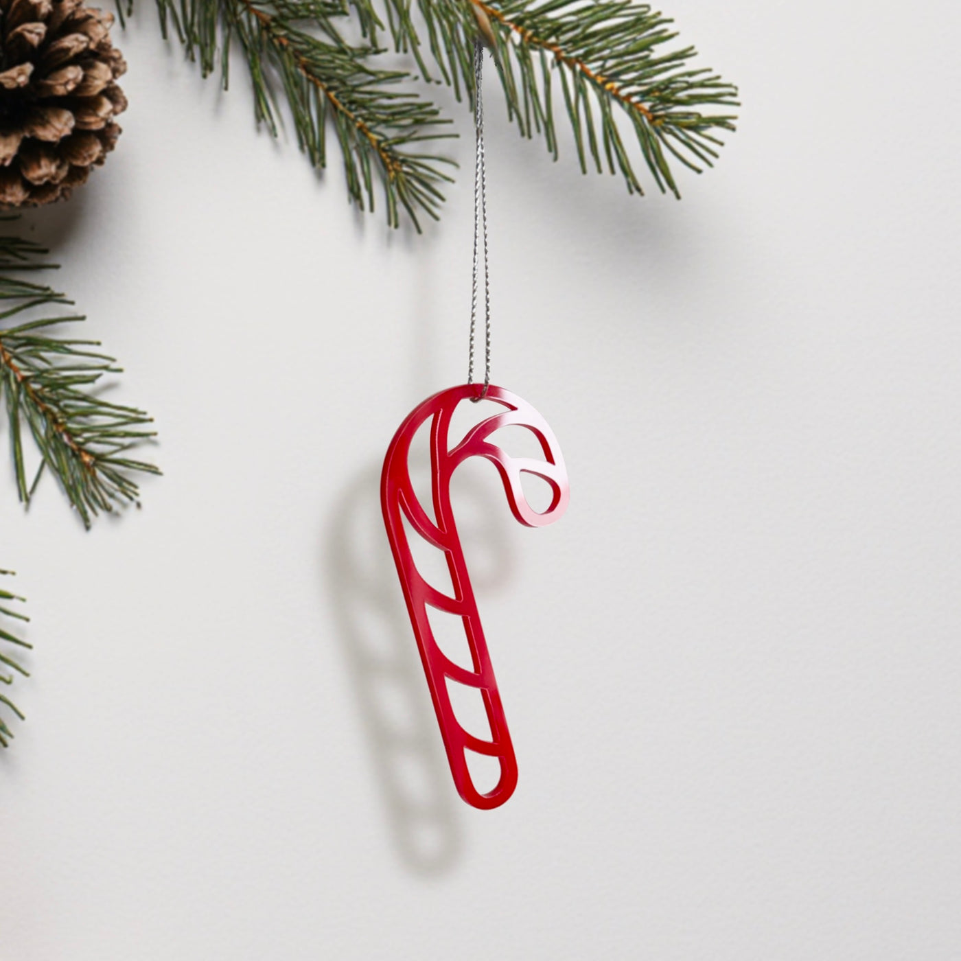 A red candy cane ornament is hanging from a branch of a pine tree.