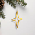 A golden star-shaped ornament is hanging from a branch of a pine tree, with pine needles and a pine cone visible in the background. - Photo #1