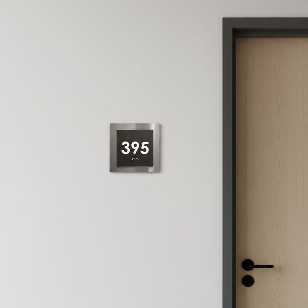 Tactile room identification sign with raised characters and Braille next to an office door
